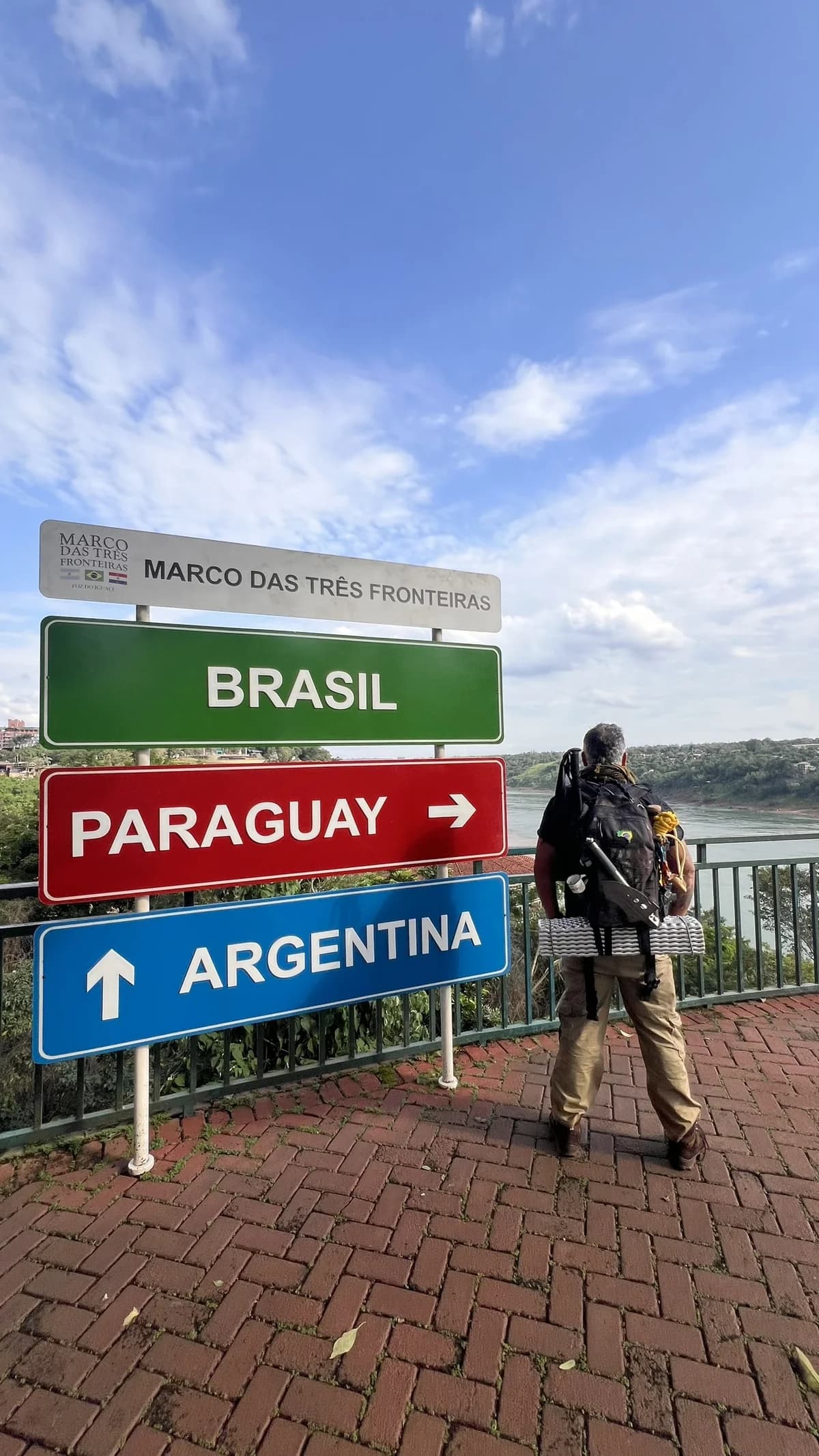 Guia Wanderlei observando as placas das três fronteiras no mirante do Marco em Foz do Iguaçu, com o rio Paraná ao fundo