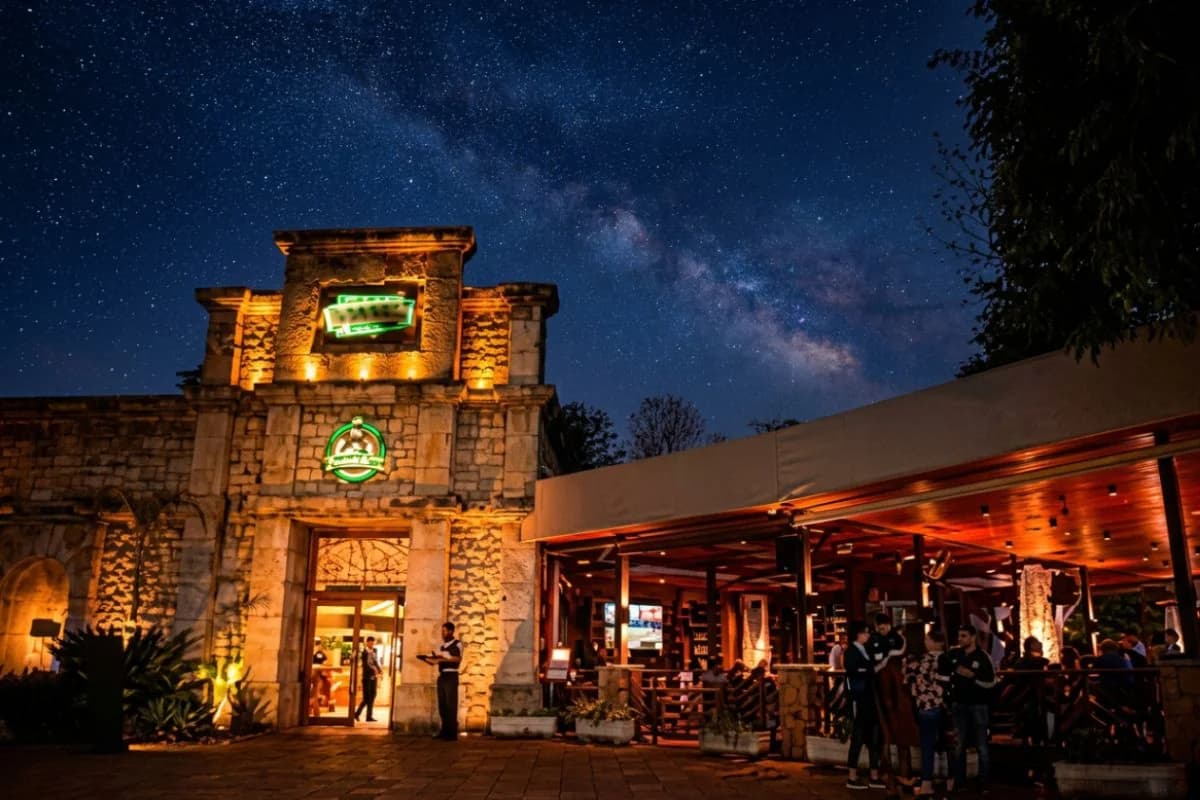 Fachada noturna do Restaurante Cabeza de Vaca no Marco das Três Fronteiras em Foz do Iguaçu, iluminada com placa neon, recepção ativa e clientes na área externa coberta — Foto: Marco das Três Fronteiras / Grupo Cataratas