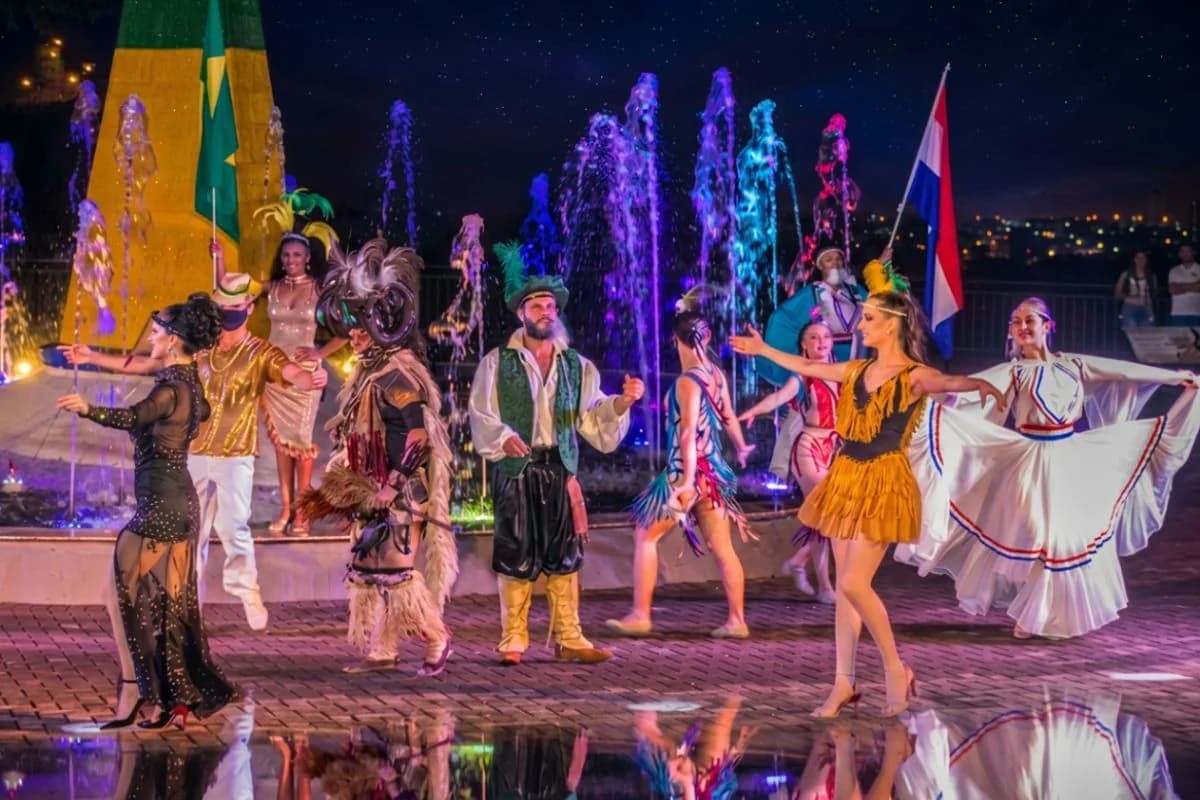 Show Três Fronteiras no Marco em Foz do Iguaçu — bailarinos representando Brasil, Argentina e Paraguai diante do chafariz iluminado — Foto: Marco das Três Fronteiras / Grupo Cataratas