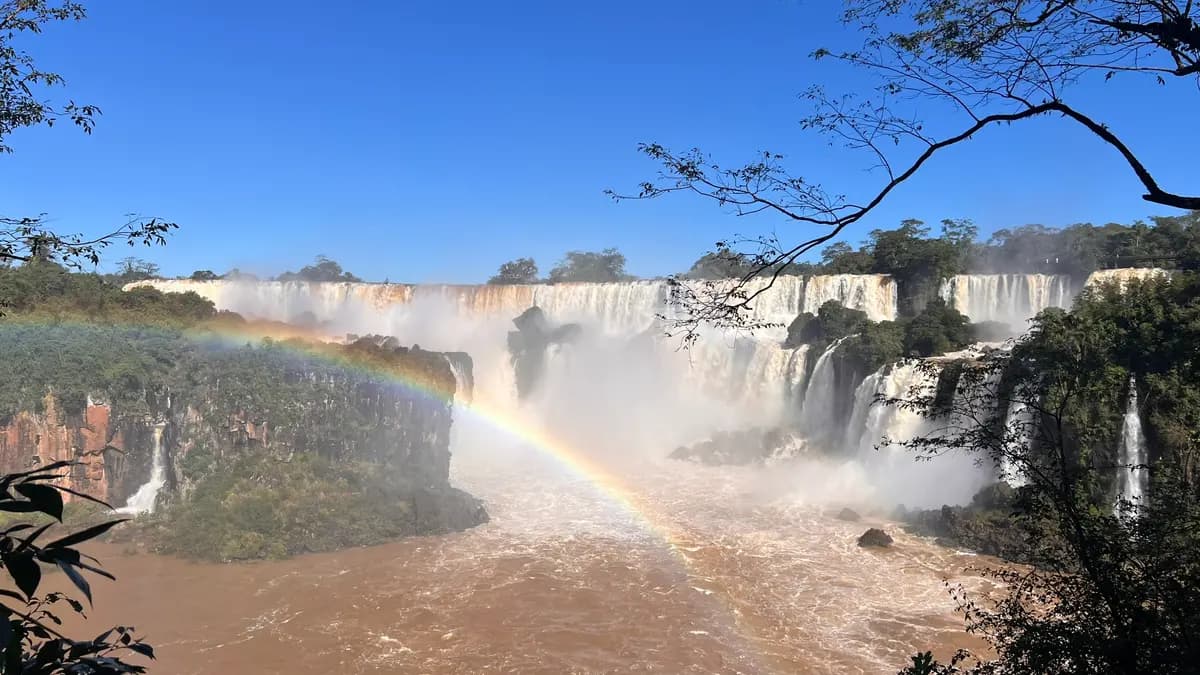 Cataratas do Iguaçu com o rio em grande volume e um arco-íris completo sobre as quedas, em dia de céu azul