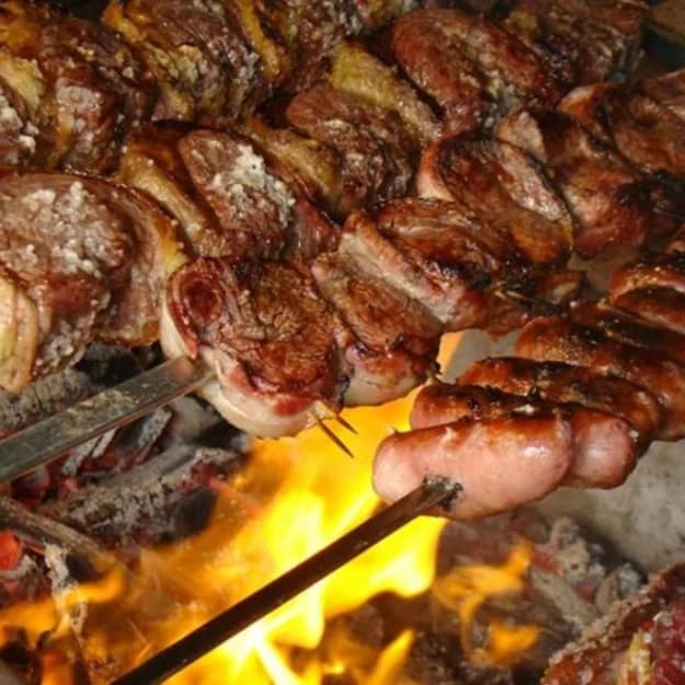 Espetos de carne assando na churrasqueira a fogo aberto do Rafain Churrascaria Show
