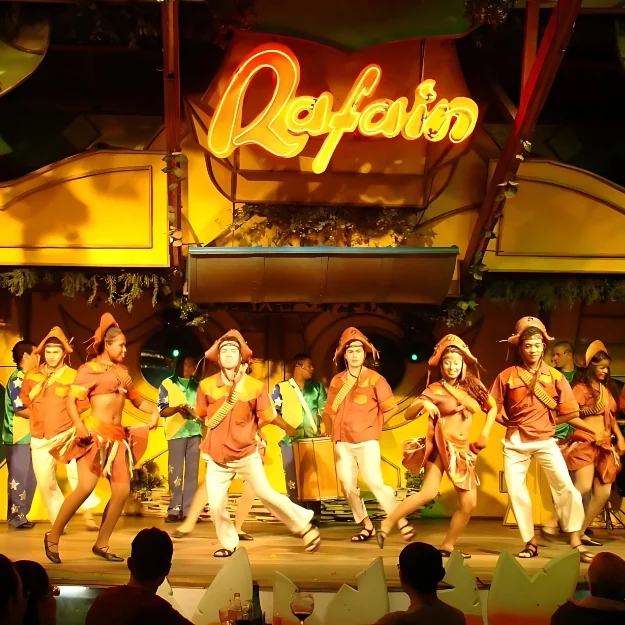 Bailarinos do Iporã Lenda Show dançando no palco do Rafain Churrascaria Show, sob o letreiro em neon da casa, em Foz do Iguaçu