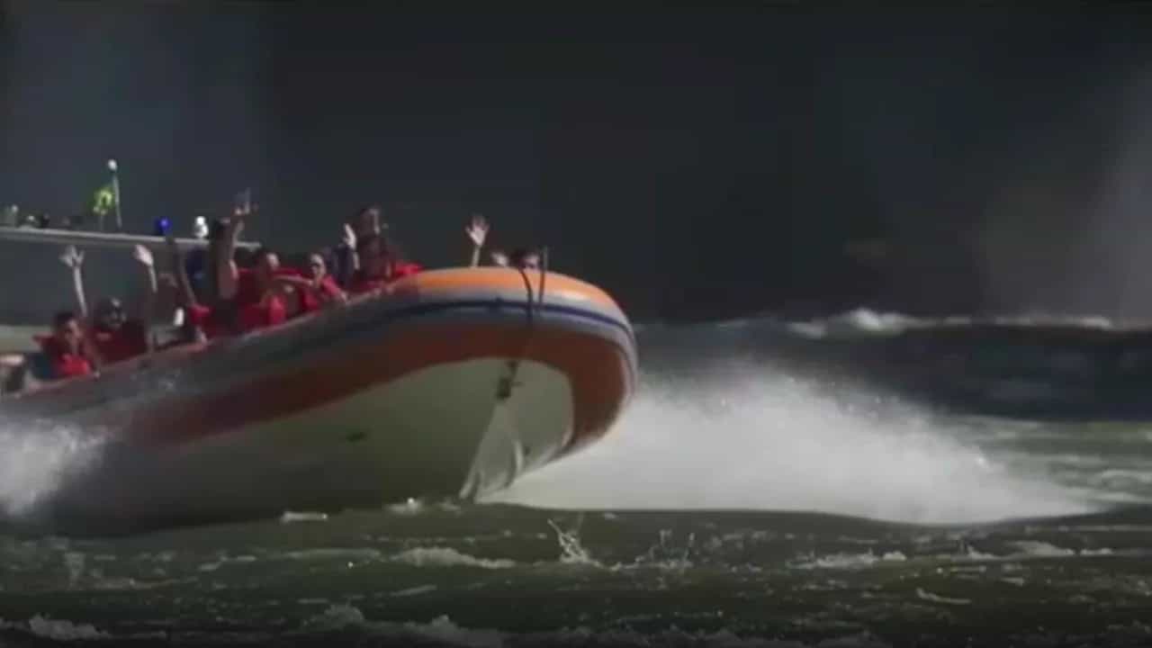 Bote do Macuco Safari em velocidade no rio Iguaçu, com passageiros de colete e braços erguidos, frame do vídeo