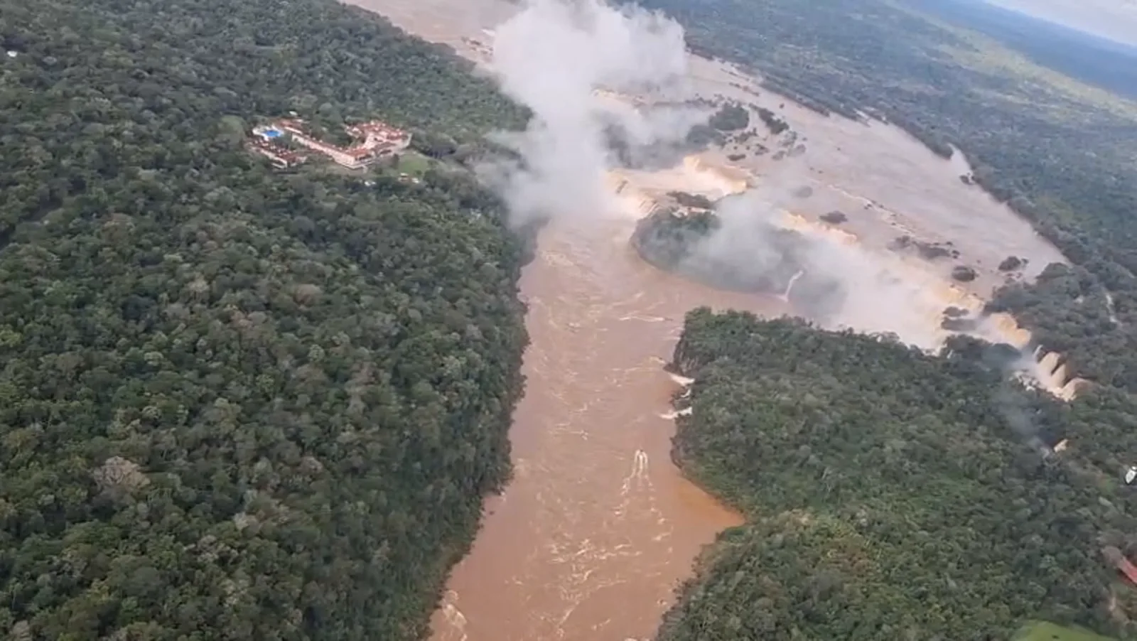 As Cataratas do Iguaçu vistas do helicóptero: o conjunto de quedas com a névoa subindo, ao lado do hotel histórico